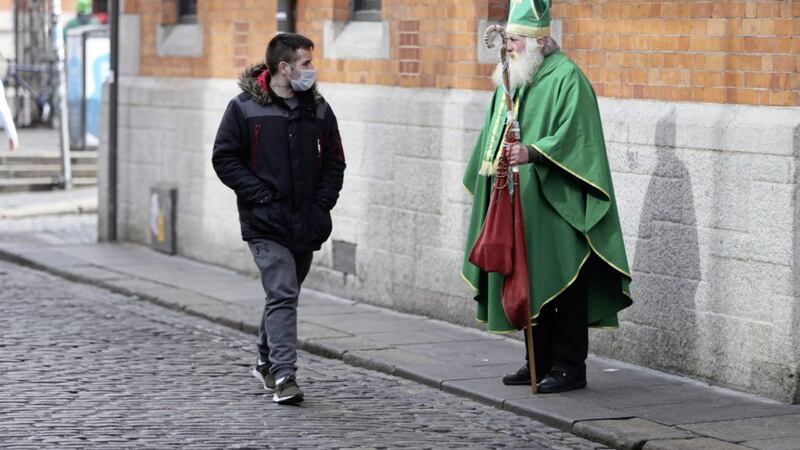 A man in a face mask walks past a man dressed as St Patrick near the Temple bar in Dublin on St Patrick&#39;s day. Picture by Niall Carson, Press Association 