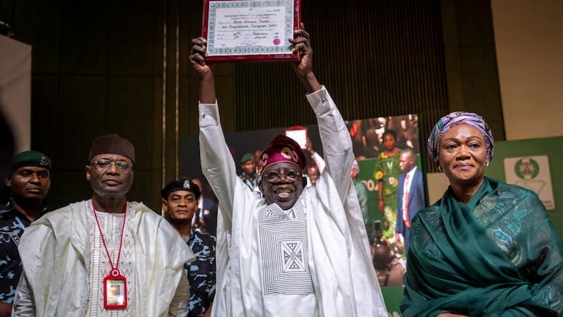 Mr Tinubu, centre, displays his certificate, accompanied by his wife Oluremi Tinubu, right, and chairman of the Independent National Electoral Commission Mahmood Yakubu, left, at a ceremony in Abuja (AP)