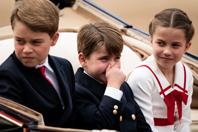 Louis holds his nose as he travels with George (left) and Charlotte in a carriage during the Trooping the Colour ceremony