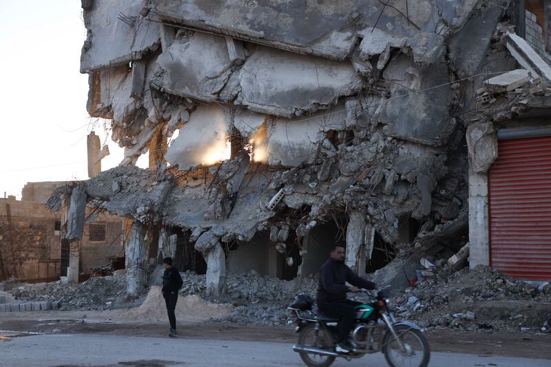 People pass a building destroyed in the February 2023 earthquake in Jinderis, Syria, which has been untouched since (Omar Albam/AP)