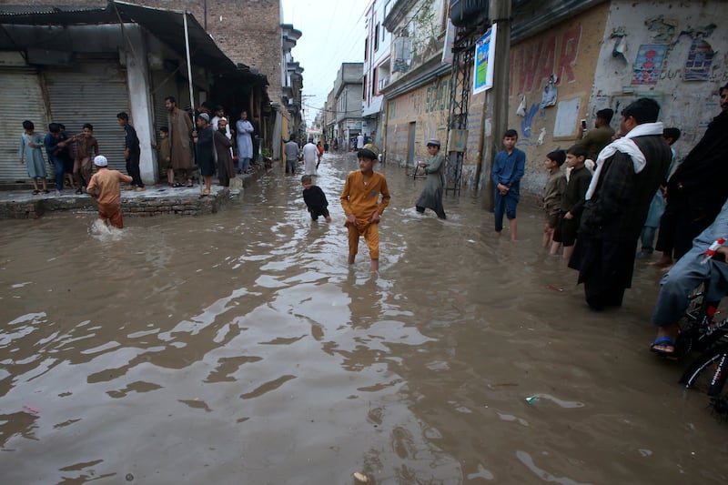 Youngsters wade through a flooded street in Peshawar (Muhammad Sajjad/AP)