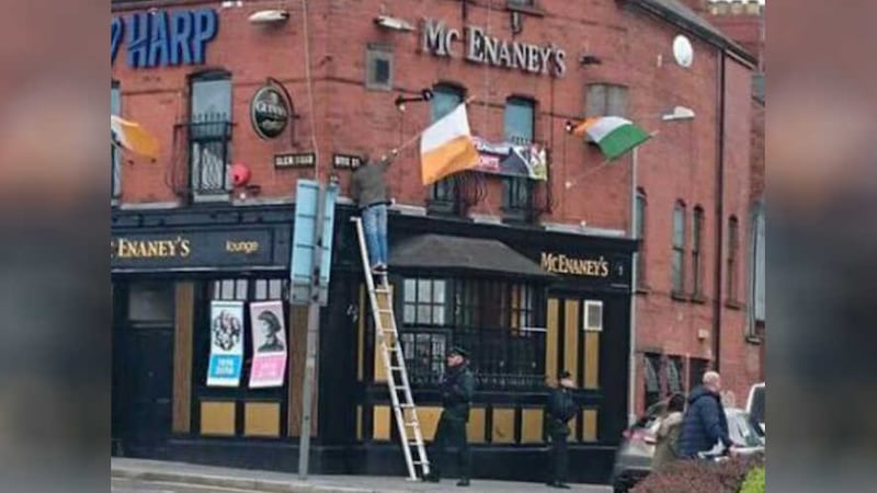 <span style="font-family: Arial, sans-serif; ">A policeman uses his foot to secure a ladder for a man erecting a tricolour outside McEnaney's bar in west Belfast on Easter Sunday</span>