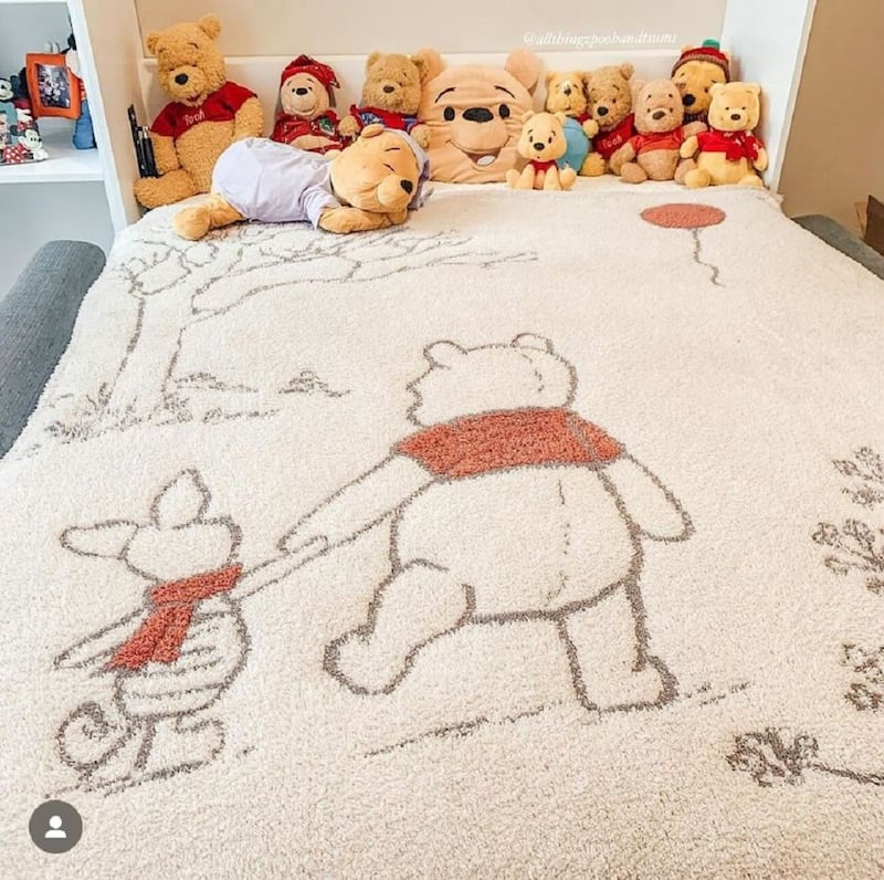 A blanket with a cartoon bear and pig on it on a bed, which is covered with stuffed bear toys