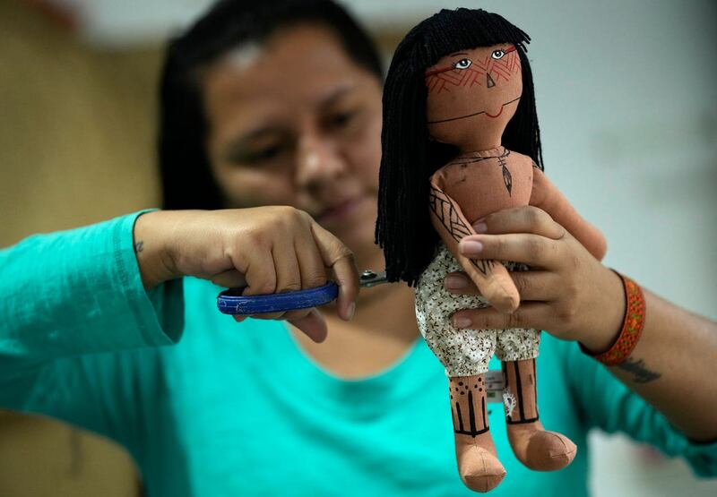 Atyna Pora, of Brazil’s Anambe indigenous group, clips the hair made of yarn of an indigenous doll, at a sewing workshop in Rio de Janeiro, Brazil 