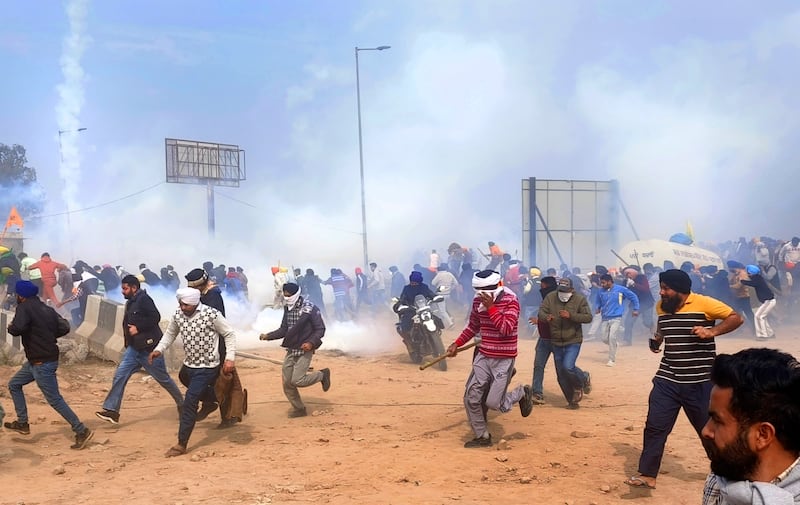 Farmers run for cover as police fire tear gas to disperse protesters (Rajesh Sachar/AP)