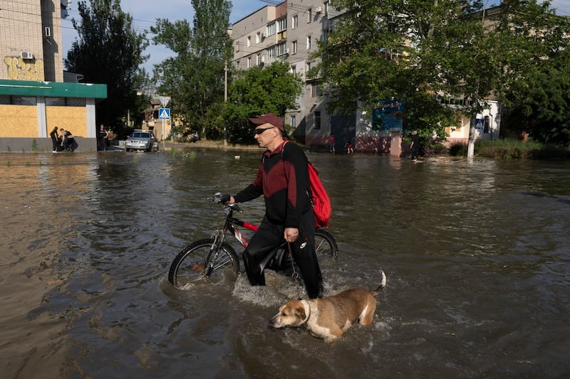 A local resident with a bike and a dog walks along the street past the buildings in Kherson, Ukraine, Tuesday, Jun 6, 2023 which were flooded after the Kakhovka dam was blown up overnight 