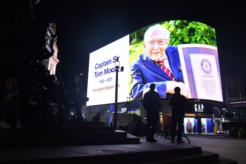 Members of the public stand in front of a tribute to Captain Sir Tom Moore at the Piccadilly Circus lights, central London, as they join in with a nationwide clap in honour of the 100-year-old charity fundraiser who died on Tuesday after testing positive for Covid-19