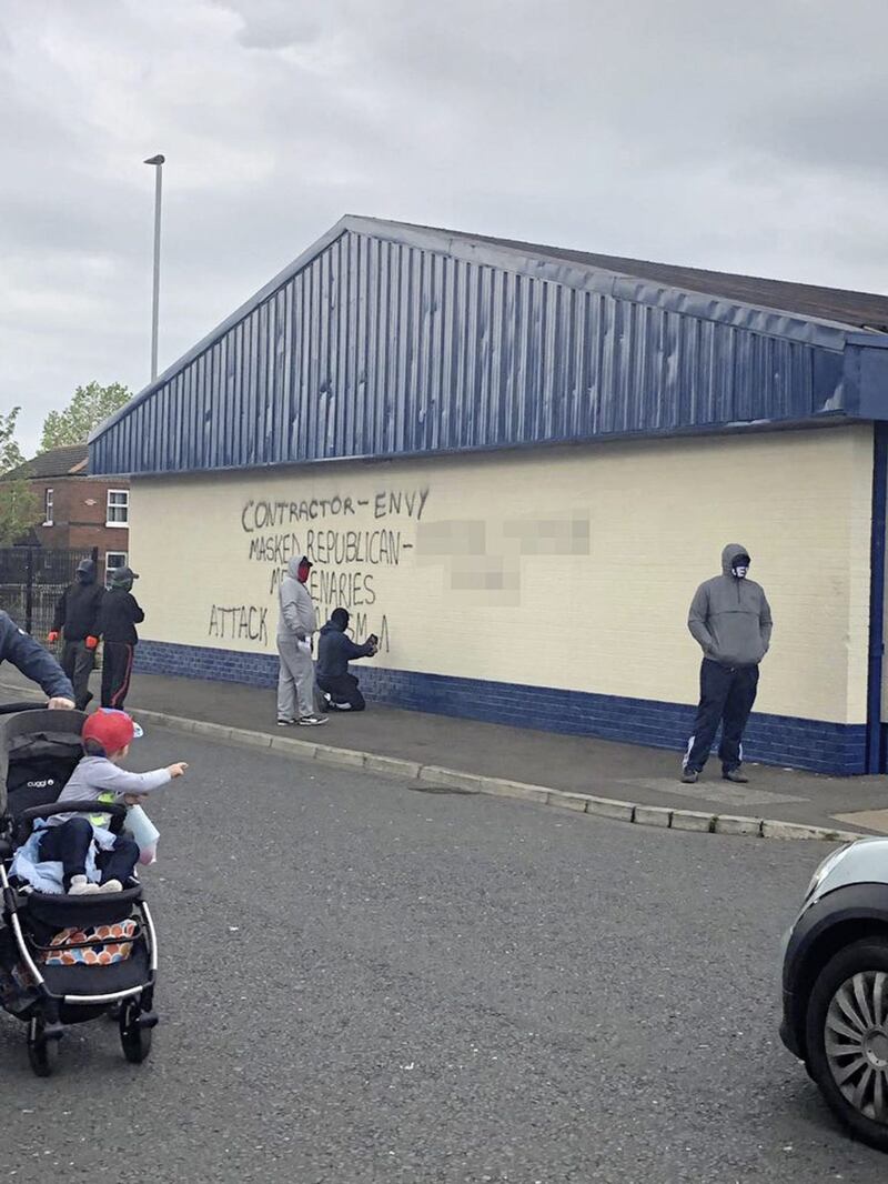 Masked men near Avoniel Leisure Centre in east Belfast spray a message on a wall naming a company they claim is involved in removal of bonfire materials 