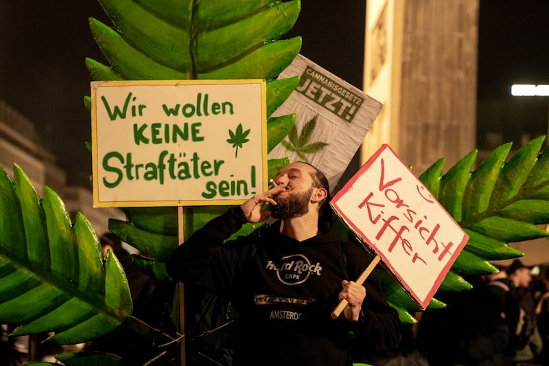 A man takes a puff from a cigarette next to a placard reading ‘We don’t want to be offenders’ in front of the Brandenburg Gate (Ebrahim Noroozi/AP)