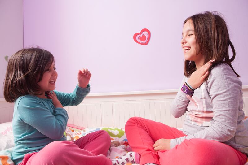 Two young girls signing to each other in a bedroom