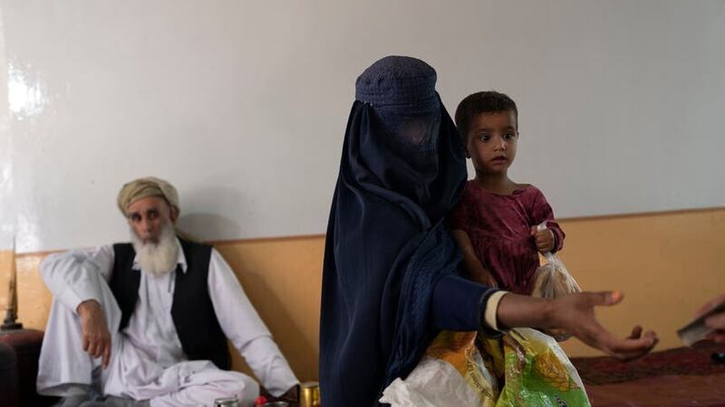 A woman begs while carrying her daughter inside a tea shop in Kabul (Rodrigo Abd/AP)
