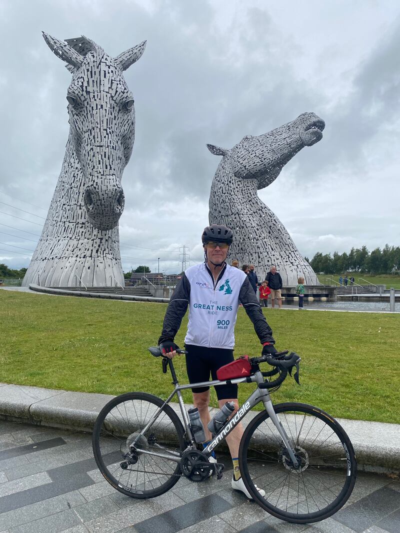 Pete Hawkins standing with his bike in front of two large statues of horse heads at The Kelpies in Falkirk