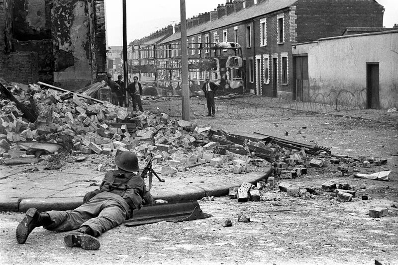 A British Army soldier lying down with a gun pointing towards a man in the Falls Road area of Belfast in 1969