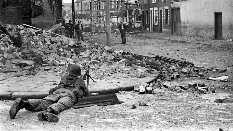 A British Army soldier lying down with a gun pointing towards a man in the Falls Road area of Belfast in 1969