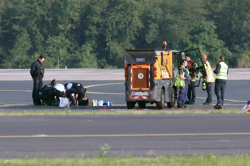 Police officers and security personnel stand on the airfield and try to detach activists of the group Last Generation who have stuck themselves to the asphalt in the airport area in Duesseldorf, Germany
