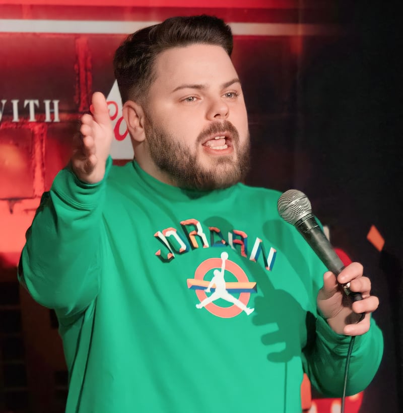 Comedian with beard and brown hair gestures on stage