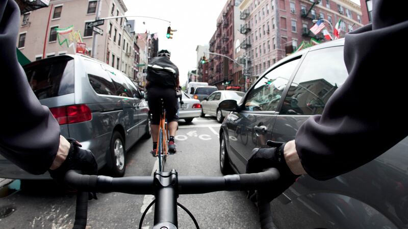 The handlebar view of a male bike courier in New York City going past cars on both sides in a traffic jam during rush hour.