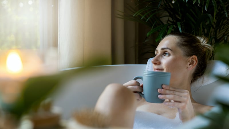 woman relaxing in bath and drink a coffee at home bathroom. looking out of window