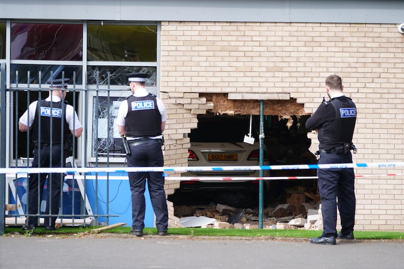 Police officers stand beside the debris and damage after a car crashed through a wall at Beacon Church of England Primary School