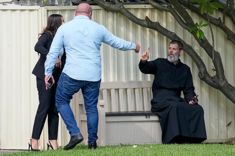 Father Daniel Kochou, right, gestures as he speaks with people, across the road from the Christ the Good Shepherd church in suburban Wakely in western Sydney (Mark Baker/AP)