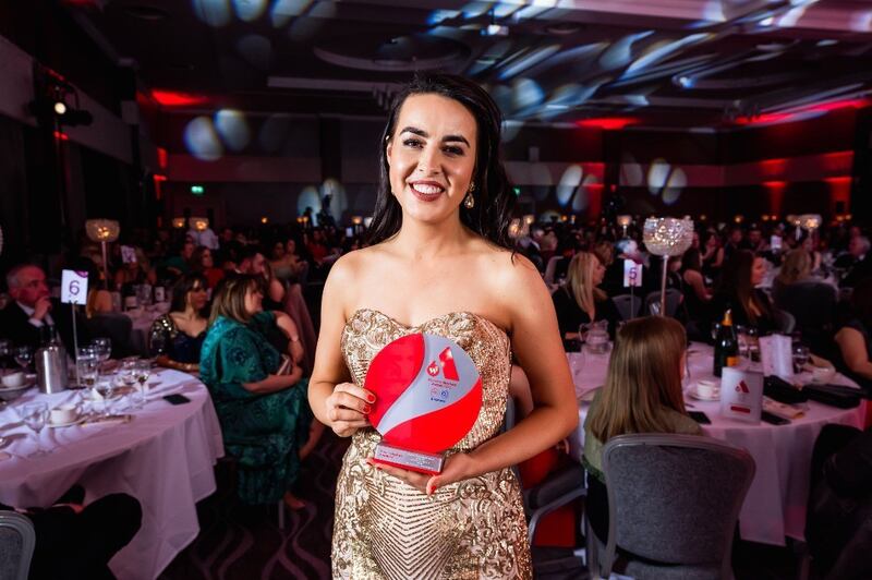 Image of Niamh McCarthy in a sparkly gold dress holding her Young Woman in business award - which is red and circular.