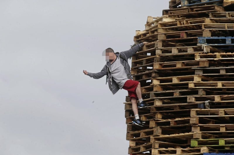 A youth clambers onto the New Lodge bonfire 