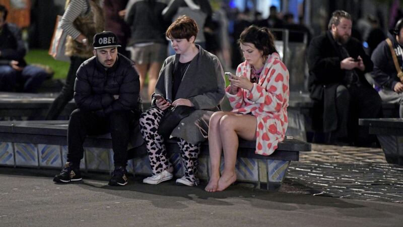 People evacuated from buildings along Dixon Street check their mobile phones while sitting on a bench in Wellington after a 6.6 earthquake based around Cheviot in the South island shock the capital, New Zealand. Picture by Ross Setford, SNPA/Associated Press