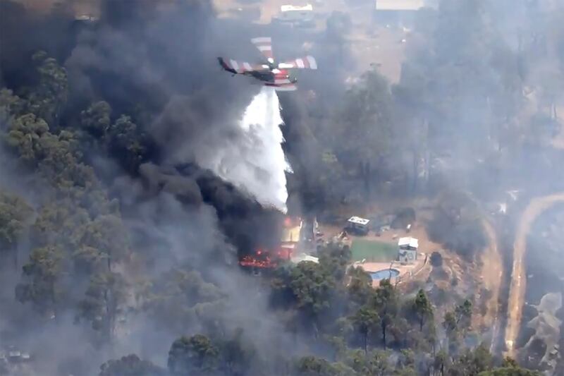 A helicopter drops water on flames billowing outside Perth, Australia (Australian Broadcasting Corp/Channel 7/Channel 9 via AP)