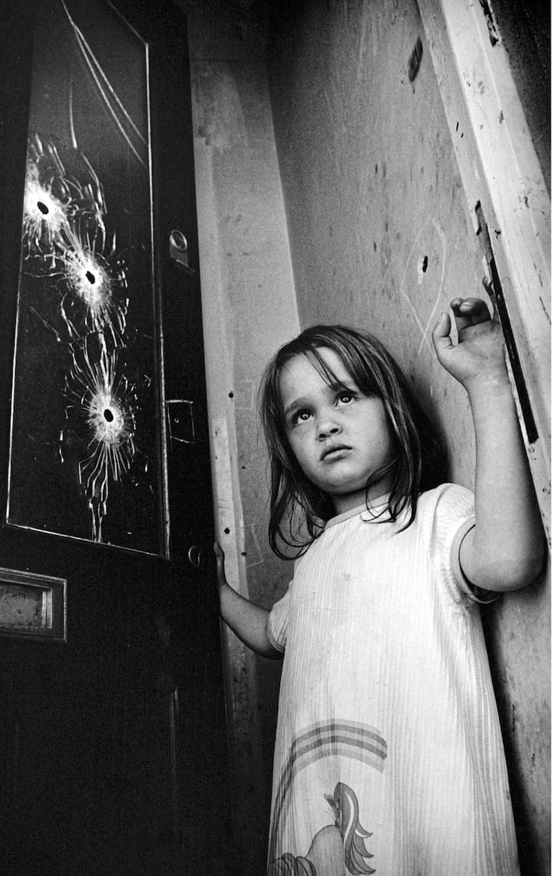 A young child by a bullet-riddled door after her home in west Belfast was attacked. Picture by Hugh Russell
