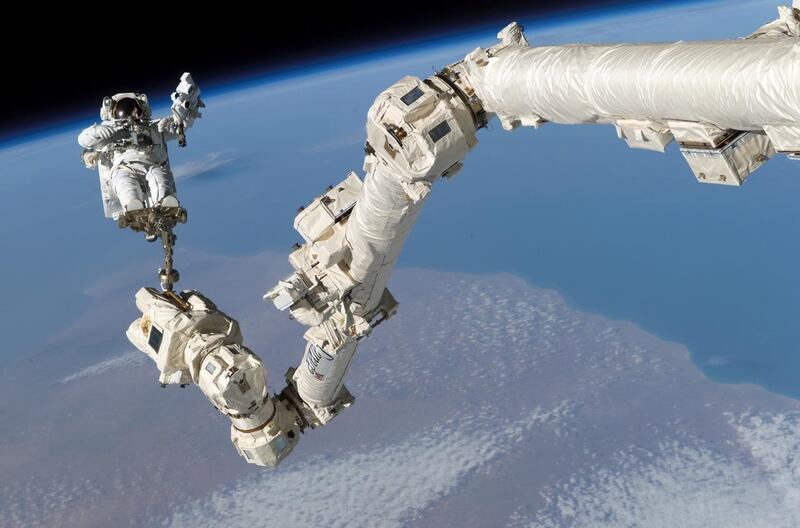 Astronaut is attached to a long arm, overlooking Earth