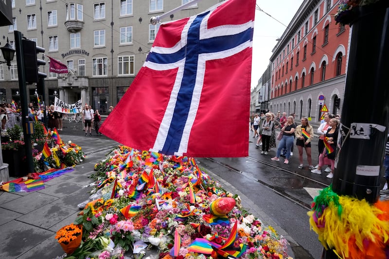 A Norwegian national flag flutters over flowers and rainbow flags that are placed at the scene of the shooting in central of Oslo, Norway on June 26 2022 (Sergei Grits/AP)