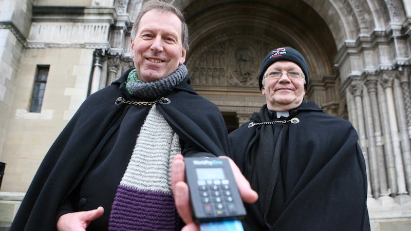 The Very Reverend John Mann and Canon Bob Jones keeping the Black Santa sit in with the times as they are now accepting credit and debit cards outside St Anne's Cathedral in Belfast. Picture by Matt Bohill&nbsp;
