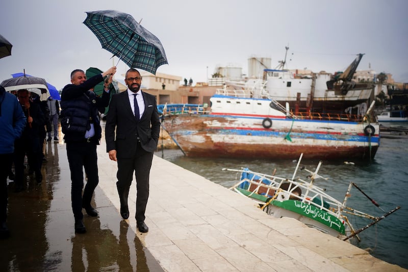 Home Secretary James Cleverly walks past a sunken boat used by migrants to cross from Africa during a visit to Lampedusa Port