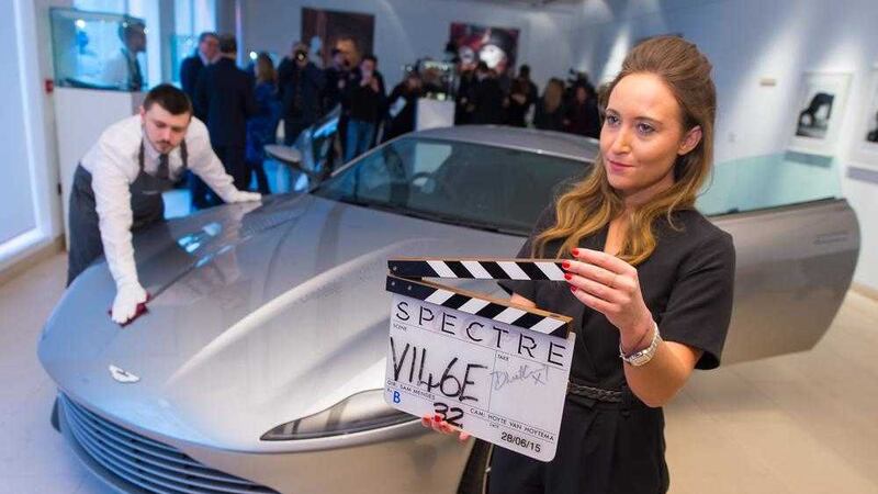 A Christies employee holds a Spectre clapper board signed by Daniel Craig alongside an Aston Martin DB10. Picture by Dominic Lipinski, Press Association