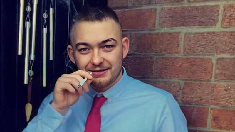 A bearded man dressed in a shirt and tie smokes a cigarette