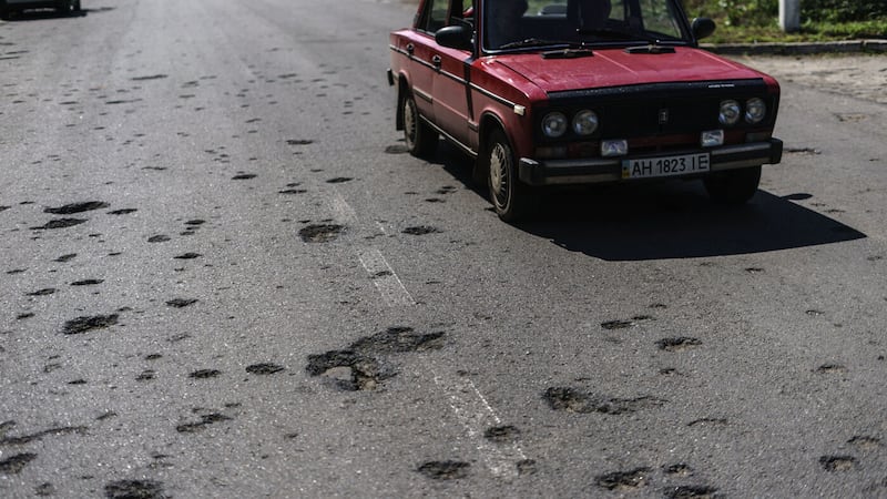 A taxi drives down a road damaged by shrapnel from a May rocket attack in Sloviansk, Donetsk region, eastern Ukraine, Saturday, Aug. 6, 2022. The echo of artillery shells thundering in the distance mingles with the din of people gathered around Sloviansk's public water pumps, piercing the uneasy quiet that smothers the nearly deserted streets of this eastern Ukrainian city. (AP Photo/David Goldman)
