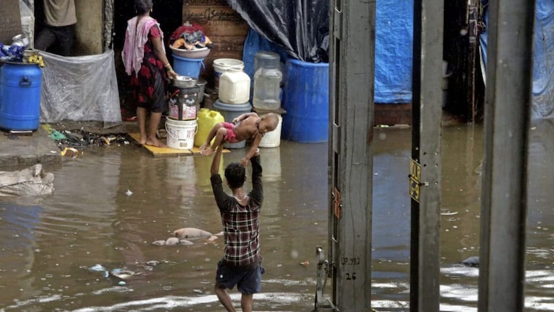 A man holds a child above his head as he wades through a waterlogged street following heavy rains in Mumbai Picture by Rajanish Kakade/AP 