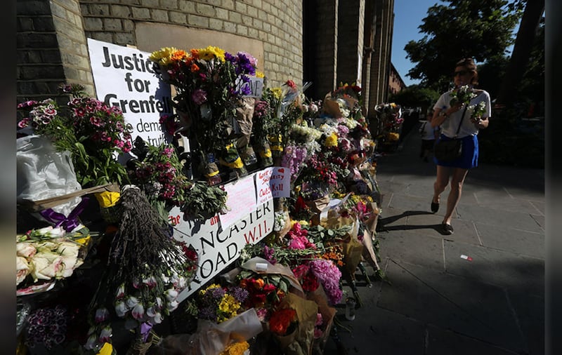 People walk past floral tributes outside Notting Hill Methodist Church, near to the Grenfell Tower in west London after a fire engulfed the 24-storey building on Wednesday morning. Picture by Jonathan Brady, PA Wire