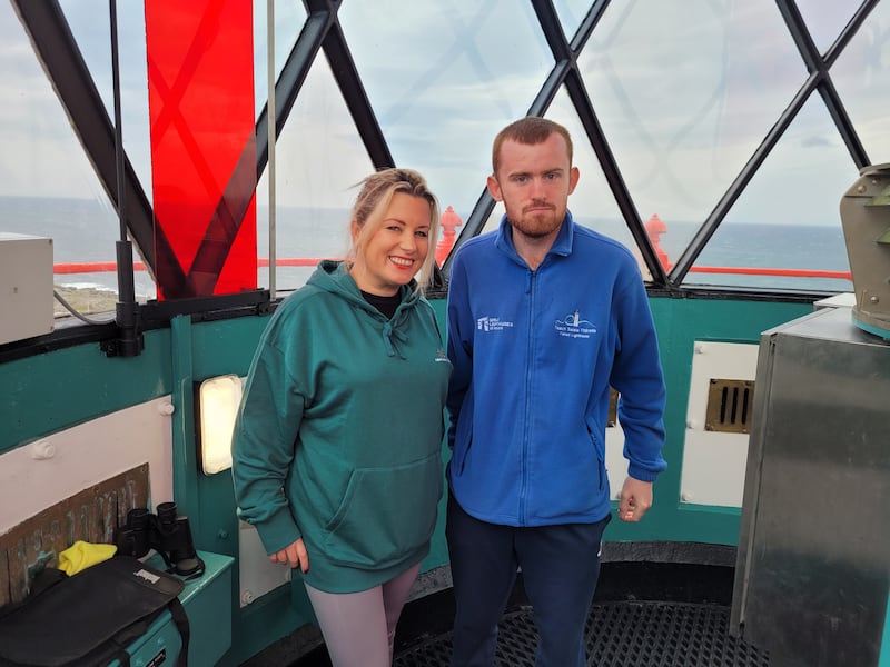 Image of blonde woman in green fleece with a man in a blue fleece standing inside a lighthouse