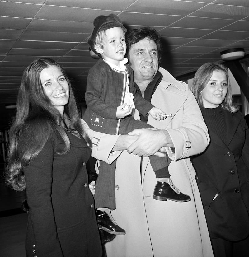 Singer Johnny Cash at London Airport carrying his son, John, with his wife, June Carter (left) and stepdaughter, Rosie