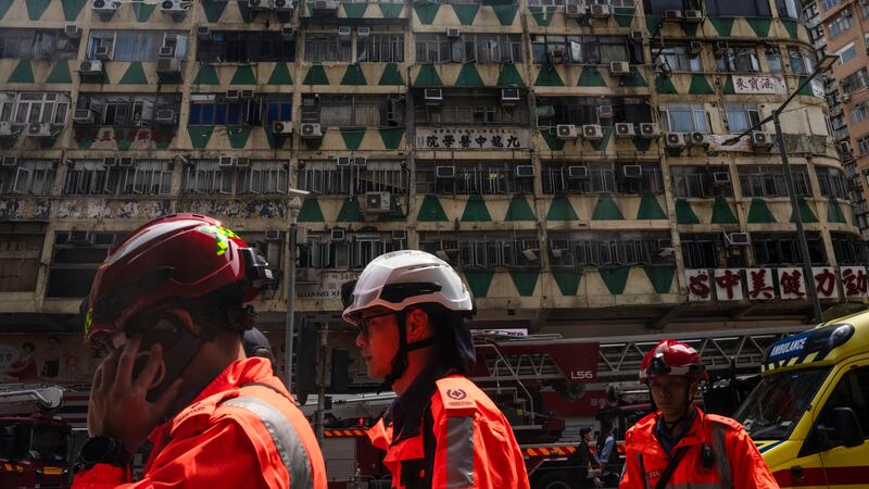 Firefighters walk past a building called New Lucky House where a fire started in Hong Kong (Louise Delmotte/AP)