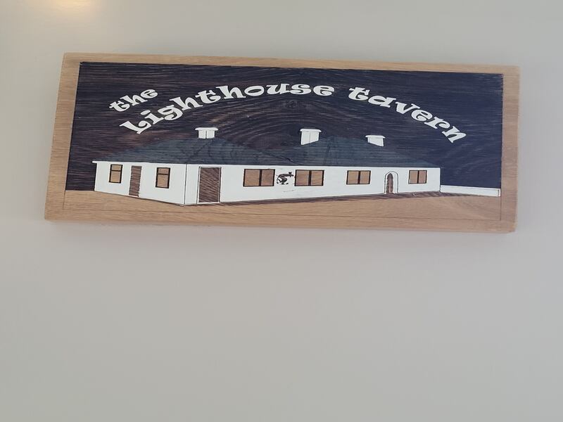 Image of a sign with a white building on it with the words The Lighthouse Tavern written on it in white