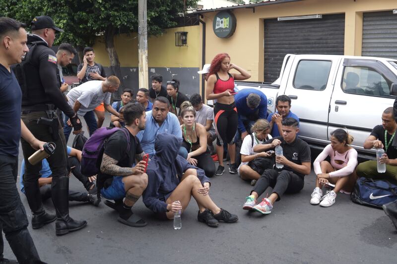 Staff members sit on a street after they were evacuated from the TC television channel station after a group of armed men broke onto their set during a live broadcast (Cesar Munoz/AP)