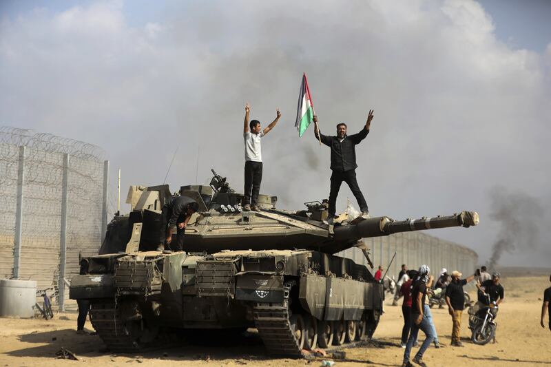 Palestinians wave their national flag and celebrate by a destroyed Israeli tank at the Gaza Strip fence (Yousef Masoud/AP)