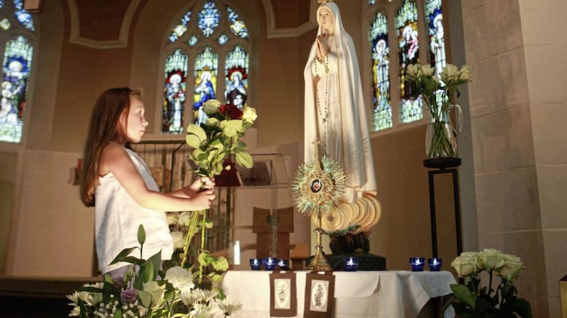 Jaime Wheelan, 8, from Belfast presents roses to Our Lady in St Teresa of Avila Church on Glen Road in Belfast during the centennial celebrations of Fatima on Sunday July 16. A pilgrim statue of Our Lady of Fatima is in Down and Connor this week. Picture by Bill Smyth.
