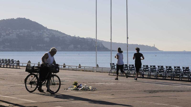 A cyclist watches flowers placed in tribute to one of the victims at the scene of a deadly attack while joggers pass by, on the famed Boulevard des Anglais in Nice. Picture by Laurent Cipriani, Associated Press