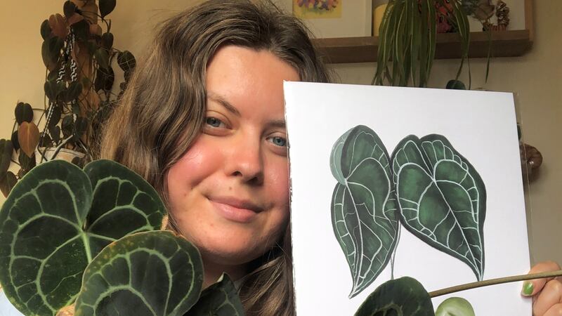 Maja Szotkiewicz holding one of her house plants in her right hand, and the artistic print of it in her left hand.