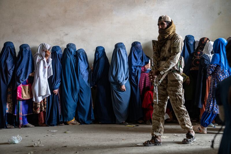 A Taliban fighter stands guard as women wait to receive food rations (Ebrahim Noroozi/AP)