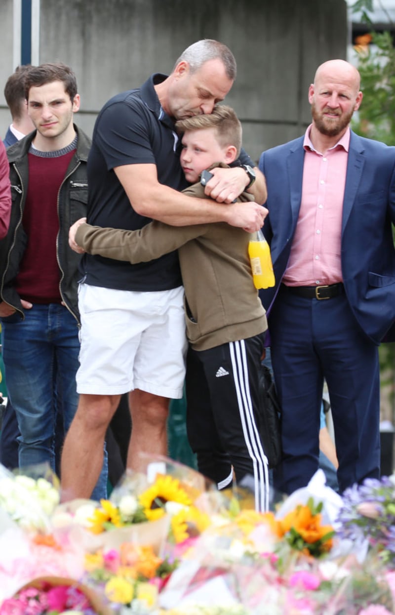 A man hugs his son after laying flowers