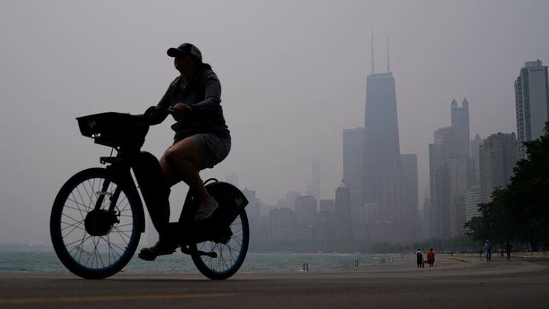 A cyclist rides a bike along the shore of Lake Michigan as the skyline is blanketed in haze (Kiichiro Sato/AP)